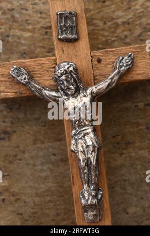 Vintage-Holzkruzifix mit silbernem Modell von Jesus Christus auf ihm, das auf angeschlagenem Metall liegt Stockfoto