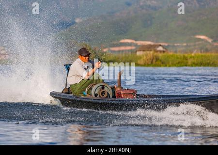 Ein birmanischer Mann mit einem starken motorisierten Schnellboot mit viel Spritzwasser vor der Natur am idyllischen Inle-See in Myanmar, Asien Stockfoto