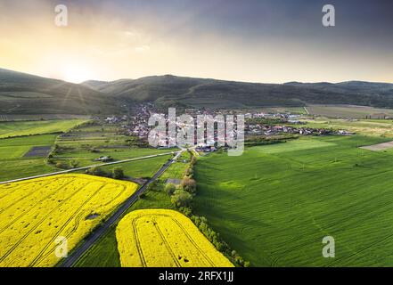 Aus der Vogelperspektive sehen Sie ein kleines Dorf mit Häusern im grünen Tal mit Bergen bei dramatischem Sonnenuntergang in der Slowakei. Stockfoto