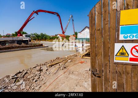 Offene Tür aus Holzbohlen mit Warnschildern, Eingang zum Gelände, Fundament des Wohngebäudes wird im Hintergrund gebaut. Stockfoto