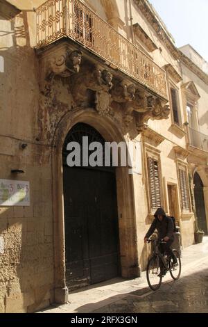 Lecce, Italien. Altes Gebäude im historischen Zentrum, mit großer Bogeneingangstür und dekorierten Korbmöbeln, die die Balkone stützen. Stockfoto