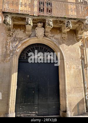 Lecce, Italien. Altes Gebäude im historischen Zentrum, mit großer Bogeneingangstür und dekorierten Korbmöbeln, die die Balkone stützen. Stockfoto