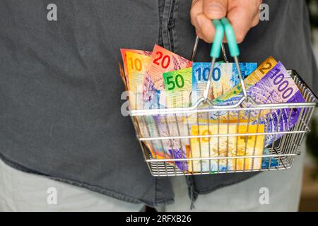 Die Schweiz, Ein Einkaufswagen voller Geld, Ein Mann mit einem Korb voller Schweizer Franken in der Hand, Finanz- und Geschäftskonzept Stockfoto