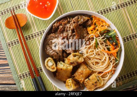 Vietnamesischer Rindernudelsalat Bun Bo mit knusprigen Frühlingsrollen und Gemüse auf dem Tisch. Horizontale Draufsicht von oben Stockfoto