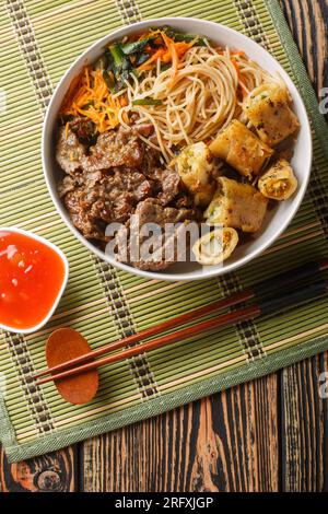 Schüssel mit traditionellem vietnamesischen Nudelsalat Bun Bo Nam Bo, mit Rindfleisch, Reisnudeln, frischen Kräutern, eingelegtem Gemüse und Fischsauce als Nahaufnahme auf dem Tisch Stockfoto