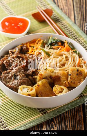 Vietnamesischer Salat mit Rind- und Sojasauce, knusprigen Frühlingsrollen und Reisnudeln, frischen Kräutern, Gemüse auf dem Tisch. Vertikal Stockfoto