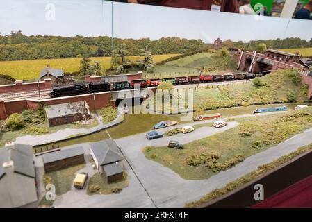 Eisenbahn des Modells N auf einer Ausstellung. Ländliche Landschaft mit Kanal und engen Booten. LMS Stanier Klasse 5 „Black Five“-Güterwagen Stockfoto