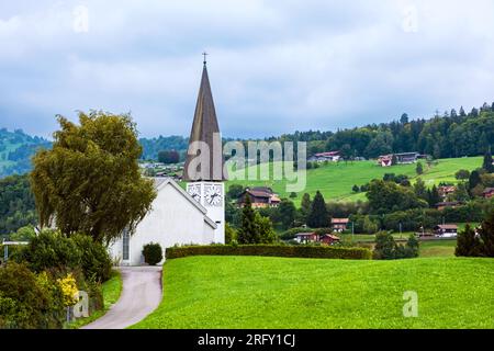 Faulensee-Dorf mit weißer Kirche und typischen schweizer Häusern auf Hügeln nahe Spiezstadt am Thunersee im Berner Oberland im Kanton Bern Stockfoto