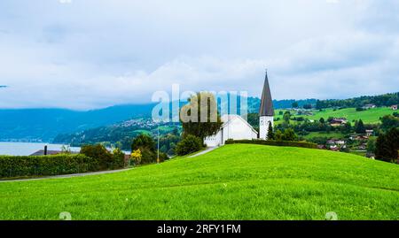 Faulensee-Dorf mit weißer Kirche und typischen schweizer Häusern auf Hügeln nahe Spiezstadt am Thunersee im Berner Oberland im Kanton Bern Stockfoto