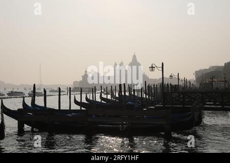 Eine Reihe leerer Gondeln in Venedig, Italien an einem trüben Tag, mit Silhouette der Basilika Santa Maria della Salute im Hintergrund Stockfoto