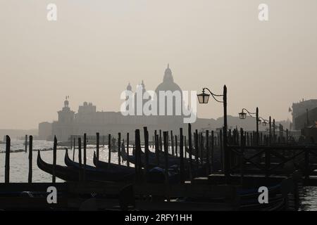 Eine Reihe leerer Gondeln in Venedig, Italien an einem trüben Tag, mit Silhouette der Basilika Santa Maria della Salute im Hintergrund Stockfoto