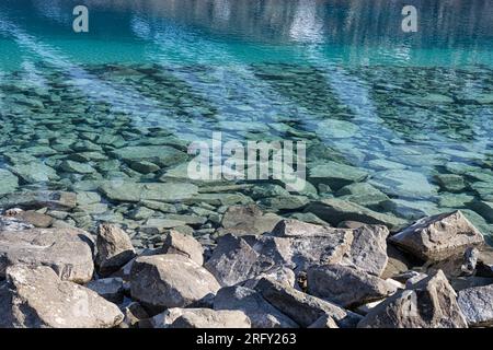 Die umliegenden, steilen, schneebedeckten Berge spiegeln sich im intensiven blauen Wasser von Blåisvatnet wider. Lyngen Alps, Troms und Finnmark, Nordnorwegen Stockfoto