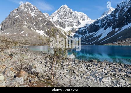 Die umliegenden, steilen, schneebedeckten Berge spiegeln sich im intensiven blauen Wasser von Blåisvatnet wider. Lyngen Alps, Troms Og Finnmark, Nordnorwegen Stockfoto