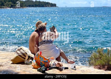 Porec, Kroatien. 06. Aug. 2023. Plava Laguna, Adriaküste in der Nähe von Porec/Kroatien, Strand. Urlauber, Paar, Paar am Steinstrand, felsiger Strand. ? Kredit: dpa/Alamy Live News Stockfoto