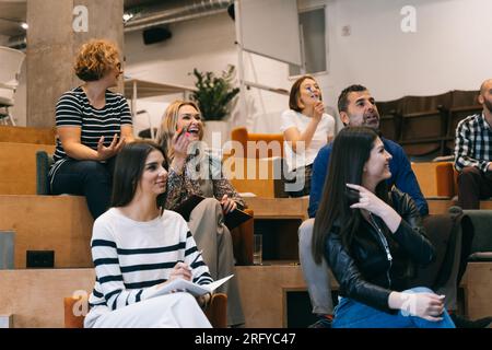 Eine Gruppe von Menschen, die sich über Generationen hinweg befanden, begann zu lachen und sprach mit ihrem Business Coach, nachdem er während der Präsentation mit ihnen scherzte Stockfoto