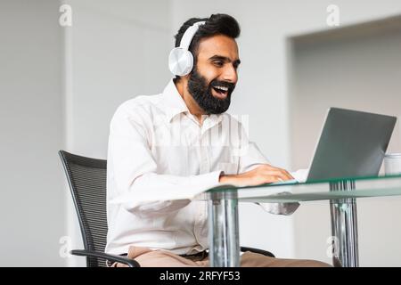 Deadline-Konzept. Lächelnder indischer Programmierer, der über einen Laptop und Kopfhörer eine Verbindung zum Internet herstellt Stockfoto