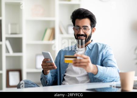 Online-Darlehen. Porträt Eines Lächelnden Indianers Mit Smartphone Und Kreditkarte Stockfoto
