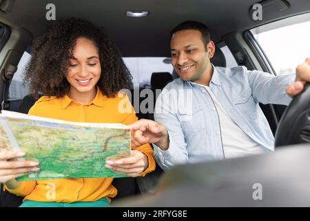 Arabischer Fahrer, der auf die Karte zeigt, in Frauenhänden im Auto Stockfoto