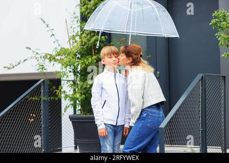 Mutter küsst ihren Sohn sanft vor der Schule. Mama begleitet ihr Kind zur Schule. Stockfoto