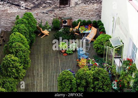 Grüner Garten mit Thujas und Blumen auf dem Dach eines Hauses in der Stadt an einem sonnigen Tag. Blick von oben Stockfoto