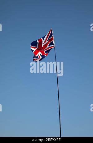 Die Unionsflagge auf einer Fahnenstange flattert in der Brise gegen einen blauen Himmel. Stockfoto