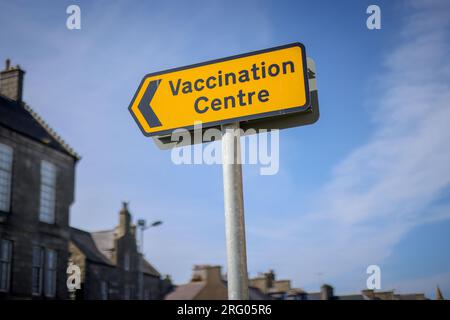 Gelbes COVID-19-Schild „Impfzentrum“ gegen blauen Himmel. Aufgenommen in Fraserburgh, Nordostschottland. Stockfoto