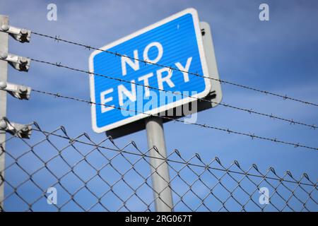 Ein „Zutritt verboten“-Zeichen, blauer Hintergrund und weißer Text. Das Schild ist hinter Stacheldraht, an einem blauen Himmel. Das wurde in einer Fischfabrik in Fraserburgh aufgenommen Stockfoto