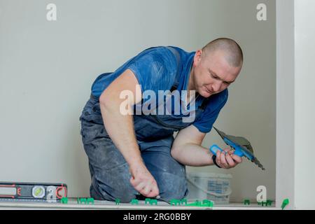 Ein männlicher Bauarbeiter installiert eine große Keramikfliese. Stockfoto