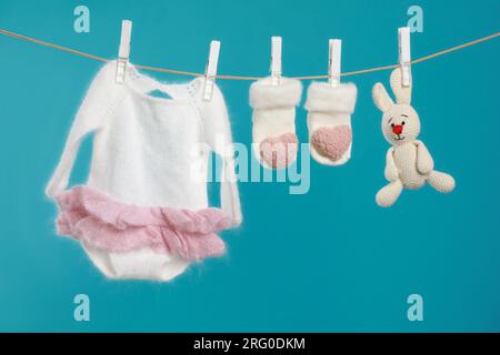 Gestrickte Babykleidung und handgemachtes Spielzeug trocknen an der Wäscheleine vor türkisfarbenem Hintergrund Stockfoto