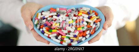 Ein Arzt mit Stethoskop hält Pillen in einer herzförmigen Schüssel. Stockfoto