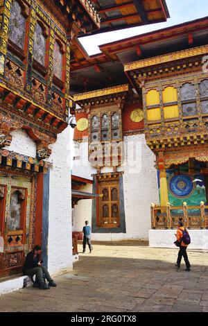 Auf dem Gelände von Punakha Dzong im Königreich Bhutan passieren Besucher kunstvoll geschnitzte und bemalte historische Gebäude aus Holz und Stein Stockfoto