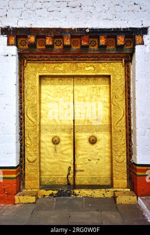 Goldene Tür mit stark geprägtem Rahmen und traditionellen Holzarbeiten oben in weiß getünchten Steinwänden in Punakha Dzong, im Königreich Bhutan Stockfoto