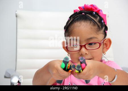 4-jähriges braunes Latina-Mädchen mit Autismus-Spektrum-Störung ASD wie Asperger, Rett und Heller zeichnet an einem Schreibtisch, spielt mit Farben allein, unsozial Stockfoto
