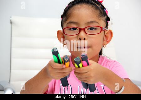 4-jähriges braunes Latina-Mädchen mit Autismus-Spektrum-Störung ASD wie Asperger, Rett und Heller zeichnet an einem Schreibtisch, spielt mit Farben allein, unsozial Stockfoto
