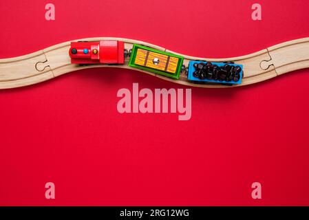 Spielzeugzug mit gebogenen Holzschienen auf rotem Hintergrund. Holzlokomotive. Stockfoto