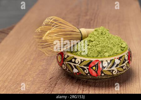 Matcha-Teepulver und Bambusquirl auf einer farbigen Keramikschüssel. Holzplanke Stockfoto