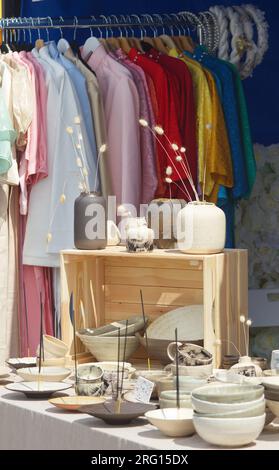 Stall mit Keramik, Schüsseln, Tassen, Vasen, Tellern und modischer Kleidung im Hintergrund auf einem Straßenmarkt in Prag Stockfoto