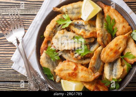 Gebratene panierte Sardellenfilets, serviert mit Zitrone und Kräutern, Nahaufnahme auf einem Teller auf dem Tisch. Horizontale Draufsicht von oben Stockfoto