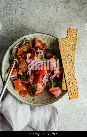 Von oben aus der Schüssel mit Salat aus Tomaten, roten Zwiebeln und Dillkraut, in der Nähe auf einem Marmortisch platziert Stockfoto