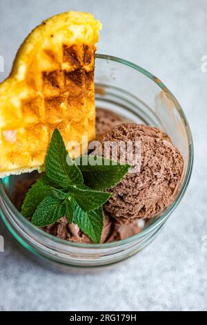 Blick von oben auf ein Glas hausgemachtes Kaffeeeis mit Waffeln und frischer Minze auf grauer Oberfläche Stockfoto