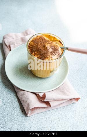 Glasbecher mit hohem Winkel und Nachtisch mit Kaffeecreme, Schokoladenpulver und Eis, serviert auf einem Teller mit Löffel auf Serviette für erfrischende Sommermahlzeiten Stockfoto
