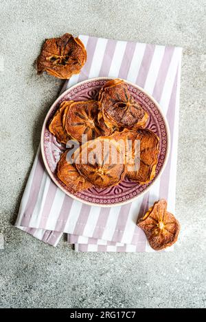 Draufsicht von Scheiben getrockneter Äpfel, serviert auf Keramikplatte auf gestreifter Serviette vor unscharfem grauen Hintergrund Stockfoto
