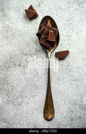Draufsicht von Stücken verschiedener Arten von Schokolade, die auf den Erntegutlöffel und auf den grau verschwommenen Tisch gelegt wurden Stockfoto