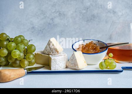 Verschiedene leckere Snacks mit verschiedenen Käsesorten und Süßigkeiten, serviert auf Keramikplatte mit Trauben Stockfoto