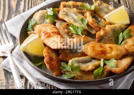 Gebratene panierte Sardellenfilets, serviert mit Zitrone und Kräutern, Nahaufnahme auf einem Teller auf dem Tisch. Horizontal Stockfoto