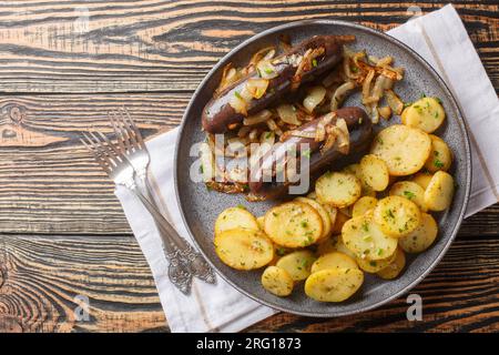 Traditioneller schwarzer Pudding mit gebratenen Zwiebeln und Kartoffeln, Nahaufnahme auf einem Teller auf dem Tisch. Horizontale Draufsicht von oben Stockfoto