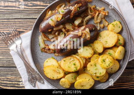 Rustikaler schwarzer Pudding mit gebratenen Kartoffeln und Zwiebeln, Nahaufnahme auf einem Teller auf dem Tisch. Horizontale Draufsicht von oben Stockfoto