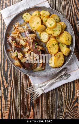 Blutwurst oder schwarzer Pudding mit gebratenen Zwiebeln und Kartoffeln auf dem Teller auf dem Tisch. Vertikale Draufsicht von oben Stockfoto