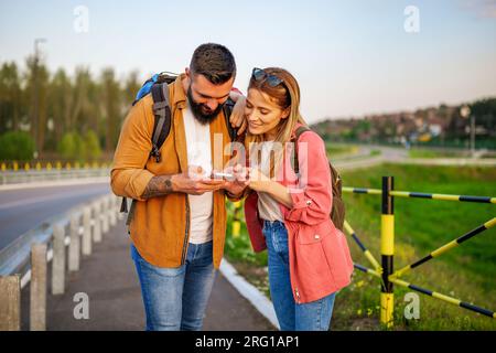 Glückliches lächelndes Paar nutzt Karten auf Smartphones in der Stadt. Touristen machen Sightseeing in der Stadt. Stockfoto