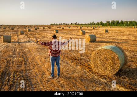 Glücklicher Bauer steht neben Heuballen. Er ist zufrieden wegen der erfolgreichen Ernte. Stockfoto